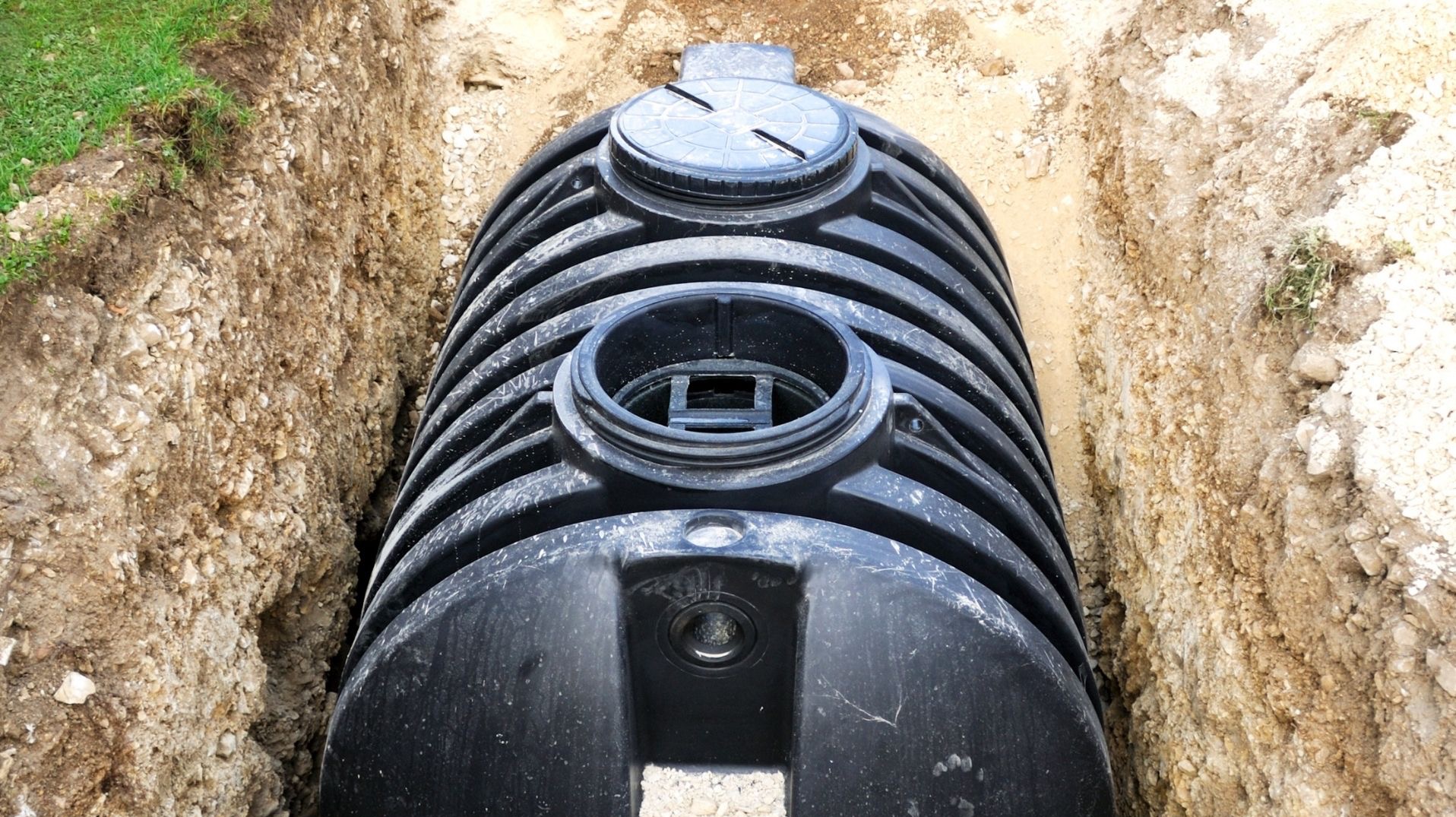 Czarny, żebrowany zbiornik z tworzywa sztucznego w wykopie ziemnym, widok z góry. Element instalacji sanitarnej, prawdopodobnie szambo lub oczyszczalnia.