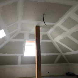 SMARTBUD - Poddasze po montażu płyt gipsowo-kartonowych z widocznymi spoinami, drewniany słup podtrzymujący konstrukcję, okno dachowe w skośnej ścianie, surowy stan.
