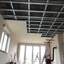 SMARTBUD - Montaż sufitu podwieszanego z płyt gipsowo-kartonowych na metalowej konstrukcji. Częściowo zamontowane płyty, widoczna izolacja poddasza.