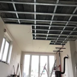 Montaż sufitu podwieszanego z płyt gipsowo-kartonowych na metalowej konstrukcji. Częściowo zamontowane płyty, widoczna izolacja poddasza.