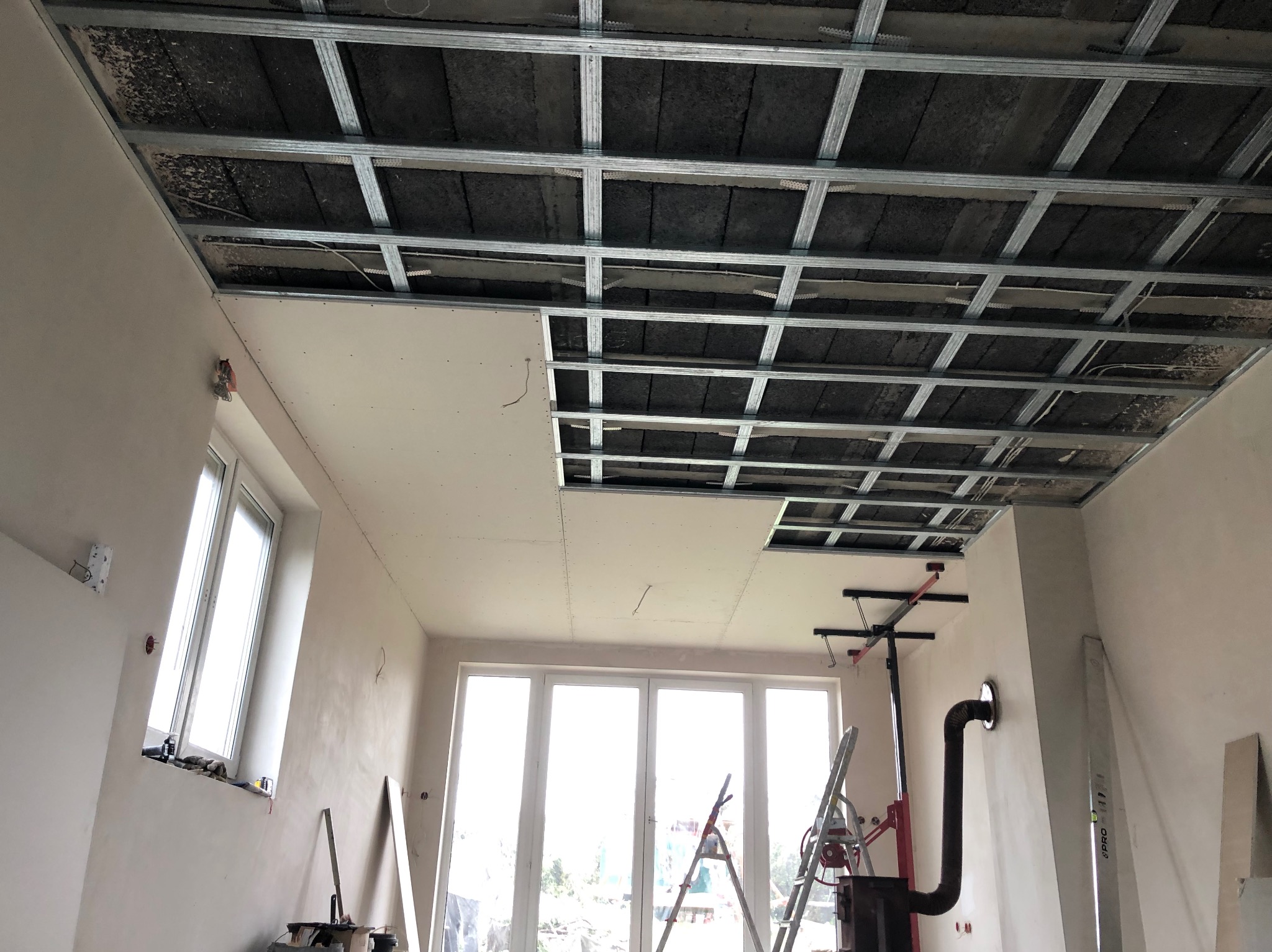 Montaż sufitu podwieszanego z płyt gipsowo-kartonowych na metalowej konstrukcji. Częściowo zamontowane płyty, widoczna izolacja poddasza.