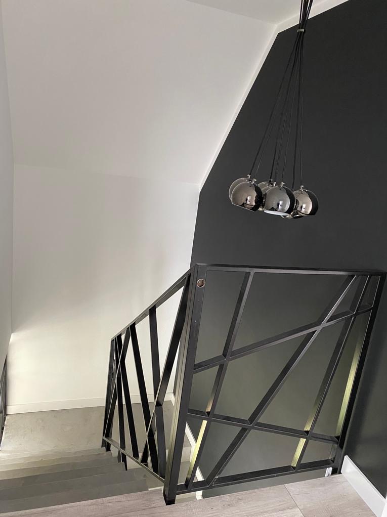 Dwukolorowa ściana (biel i grafit) z nowoczesną lampą kulistą i metalową balustradą schodową o geometrycznym wzorze, widok z góry.