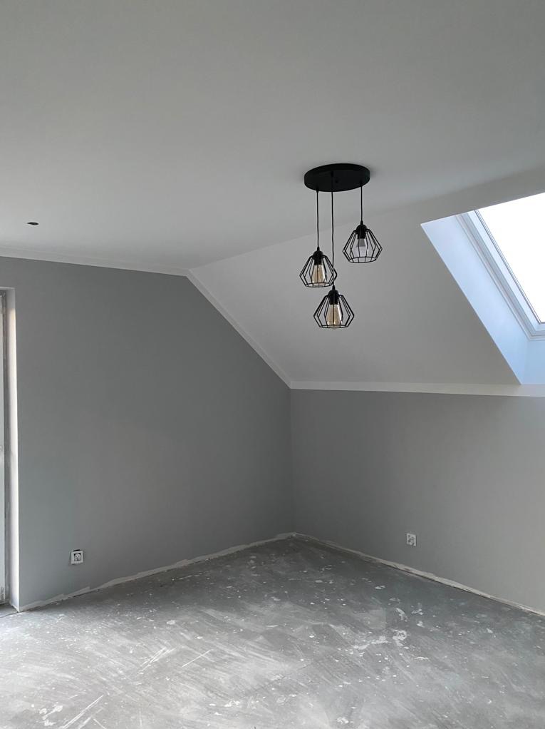 Wnętrze po malowaniu na szaro z nowoczesną lampą wiszącą. Widoczne gładkie ściany, okno dachowe i przygotowana podłoga. Minimalistyczny design.