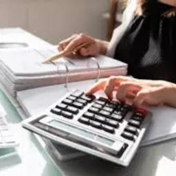 Księgowa w Wadowicach kalkuluje dane finansowe na kalkulatorze biurowym, analizując dokumenty. Widok z góry na biurko.