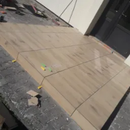 Układanie płytek imitujących drewno na tarasie, widoczne kliny poziomujące, narzędzia glazurnicze w tle. Etap prac wykończeniowych na zewnątrz budynku.