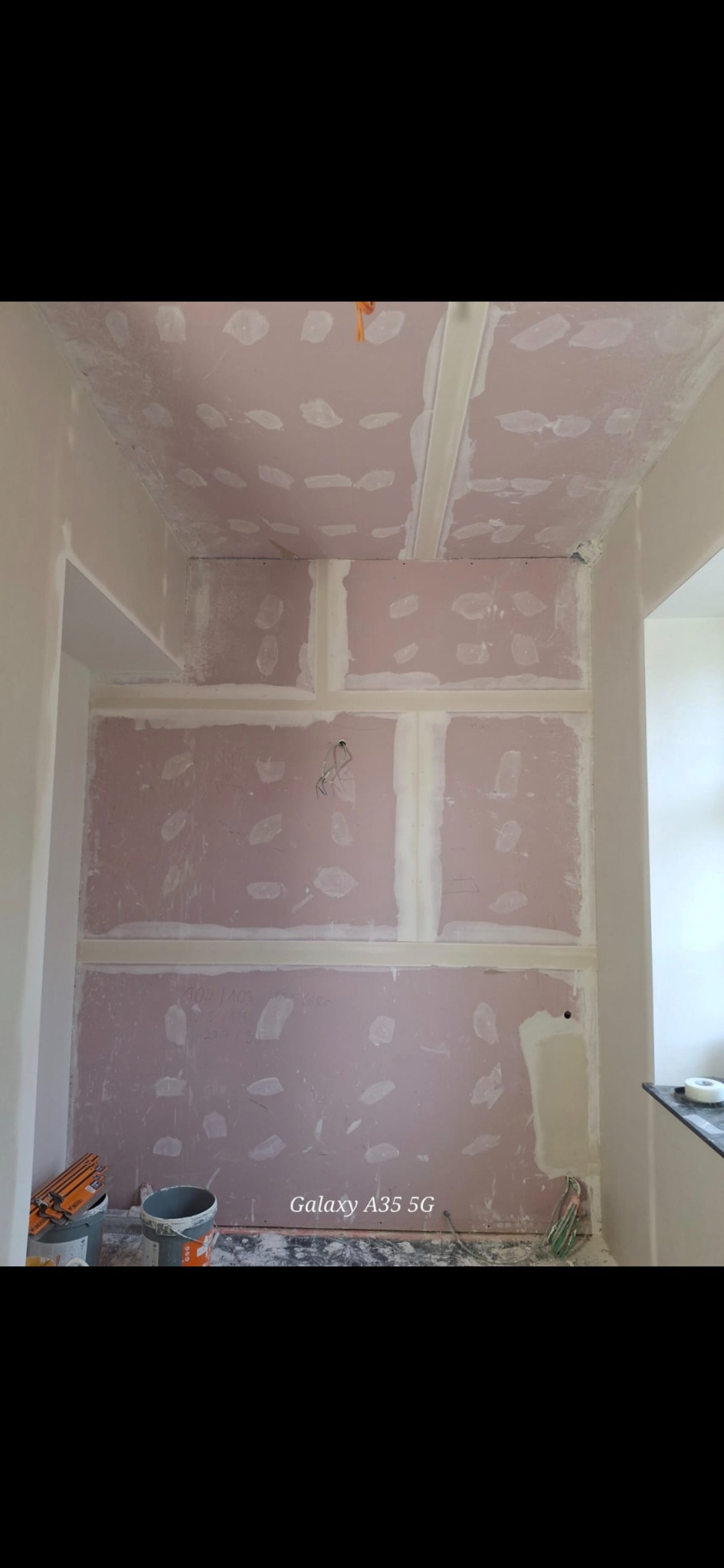 Montaż płyt karton-gips na ścianach i suficie w pomieszczeniu. Widoczne łączenia płyt wypełnione masą szpachlową. Przewody elektryczne wystają ze ściany.