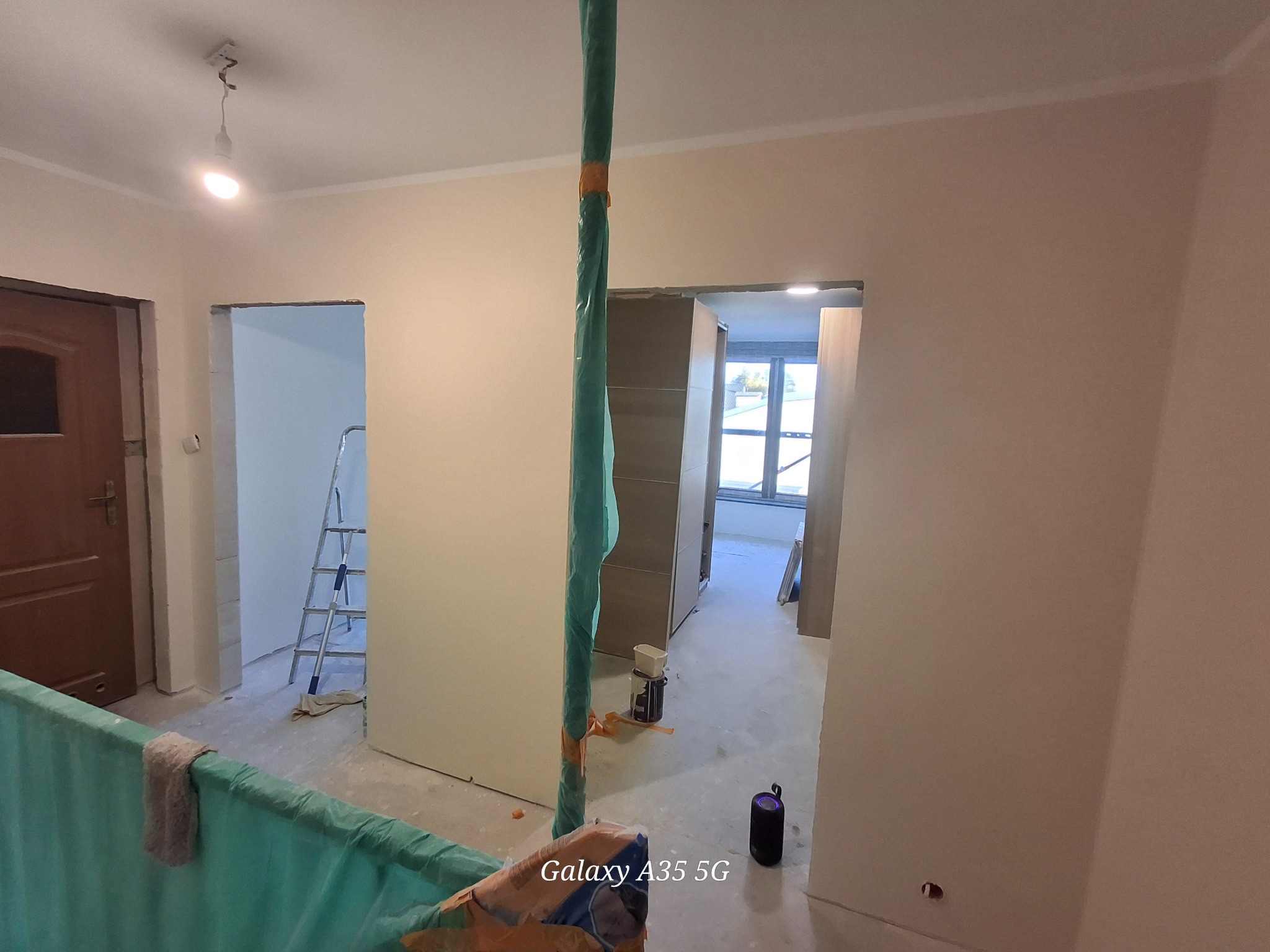 Wnętrze w trakcie prac wykończeniowych: ściany po szpachlowaniu, zabezpieczone elementy, drabina w tle. Widoczne ślady prac remontowych na podłodze.