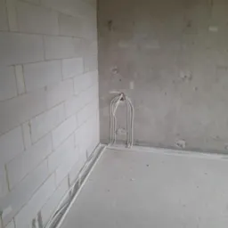 Surowy stan: Instalacja elektryczna w nowym budynku z białymi kablami ułożonymi wzdłuż ściany z betonu komórkowego i surowego tynku, przygotowanie do dalszych prac.