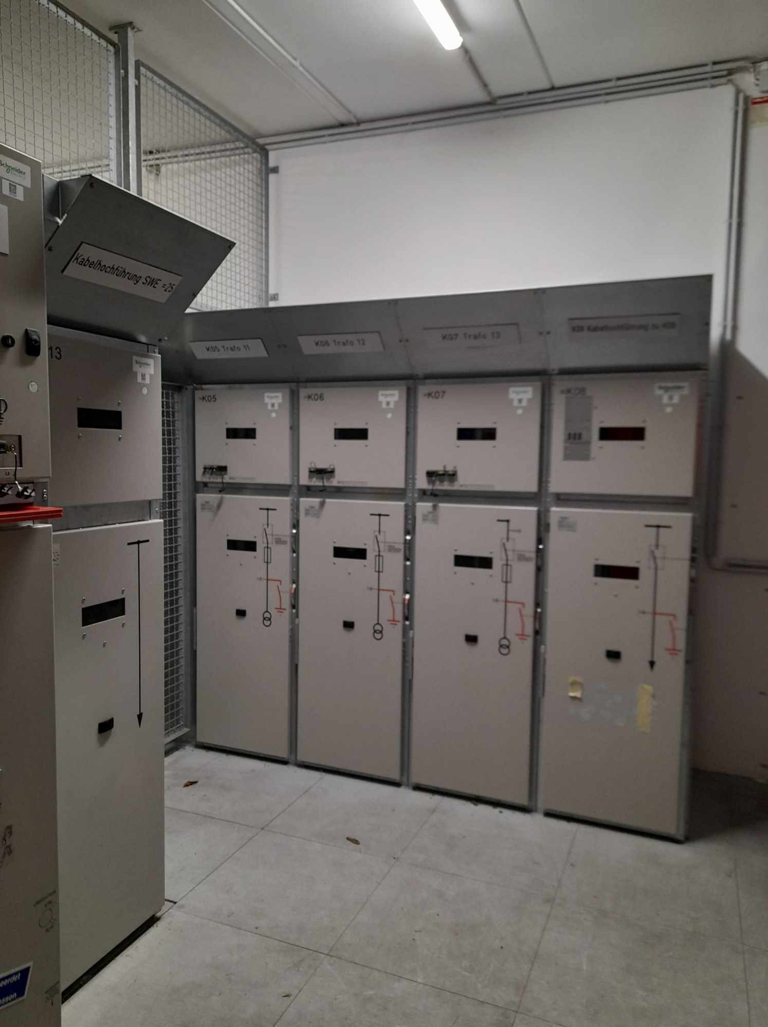 Rozdzielnia elektryczna z oznaczeniami K05, K06, K07 i K08. Widoczne schematy elektryczne na drzwiach. Szara metalowa obudowa w pomieszczeniu technicznym.