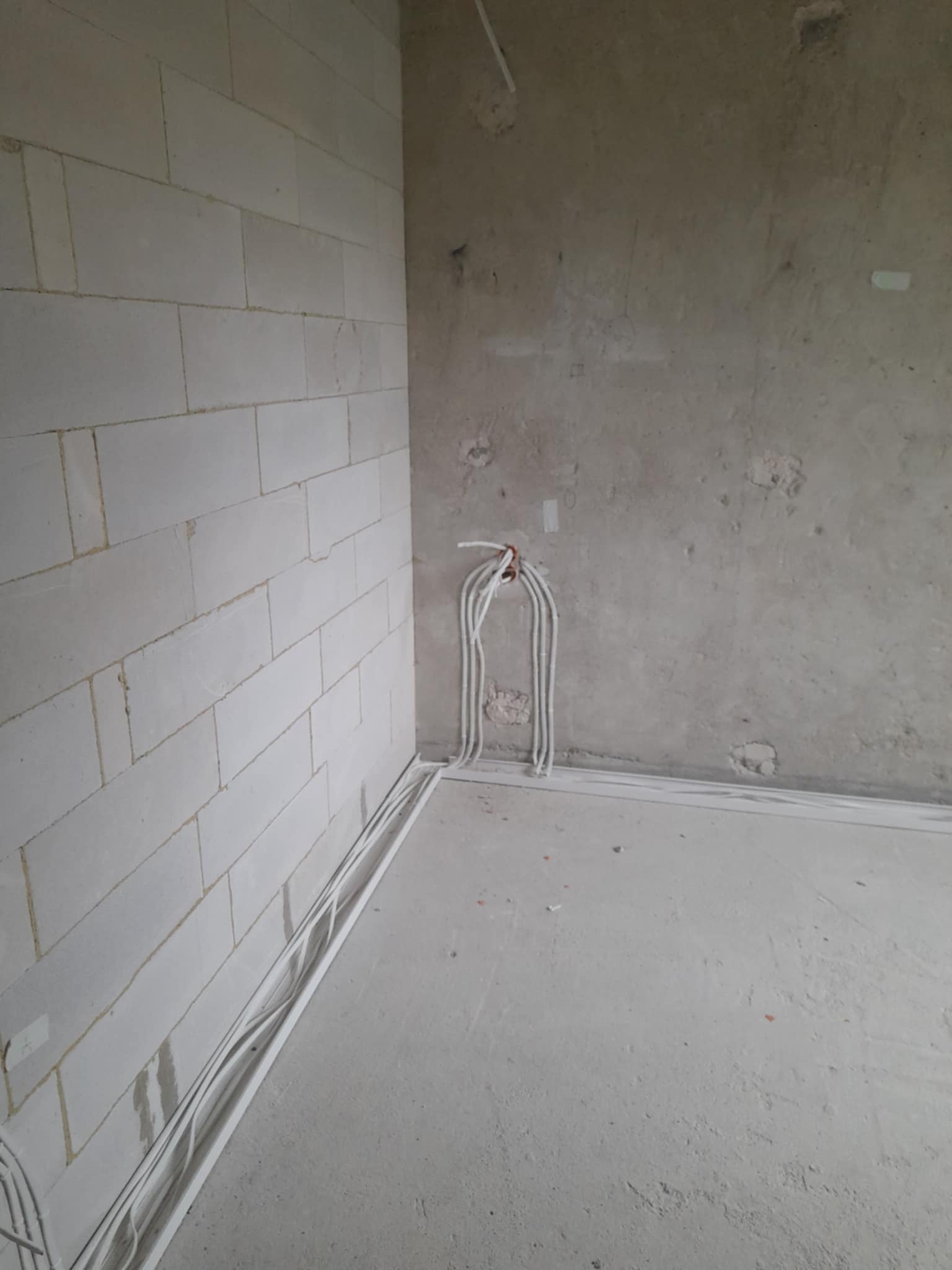 Surowy stan: Instalacja elektryczna w nowym budynku z białymi kablami ułożonymi wzdłuż ściany z betonu komórkowego i surowego tynku, przygotowanie do dalszych prac.