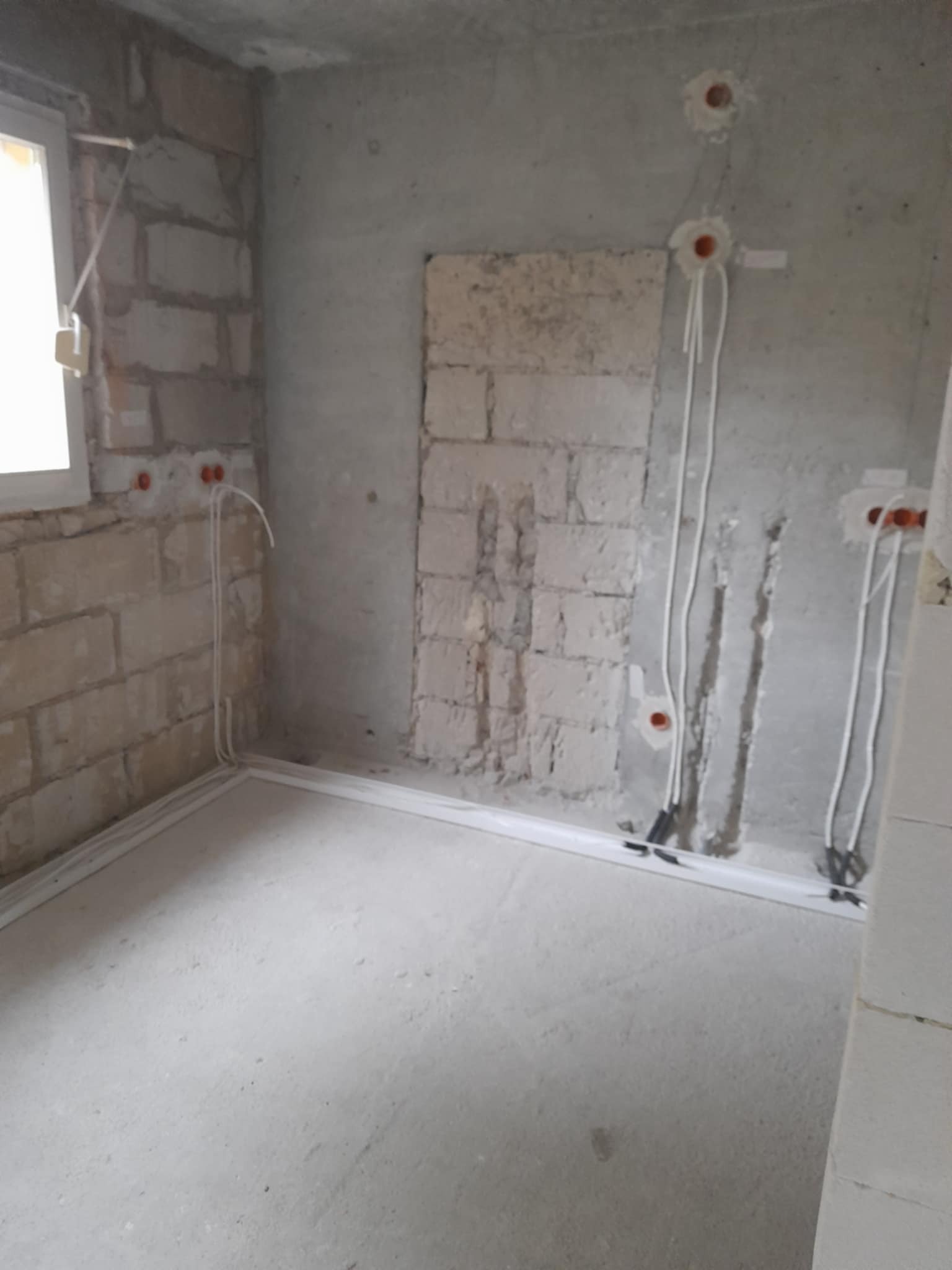 Surowy stan: ściany z cegły i betonu z częściowo poprowadzonymi przewodami elektrycznymi w białych listwach, przygotowane do dalszych prac wykończeniowych.