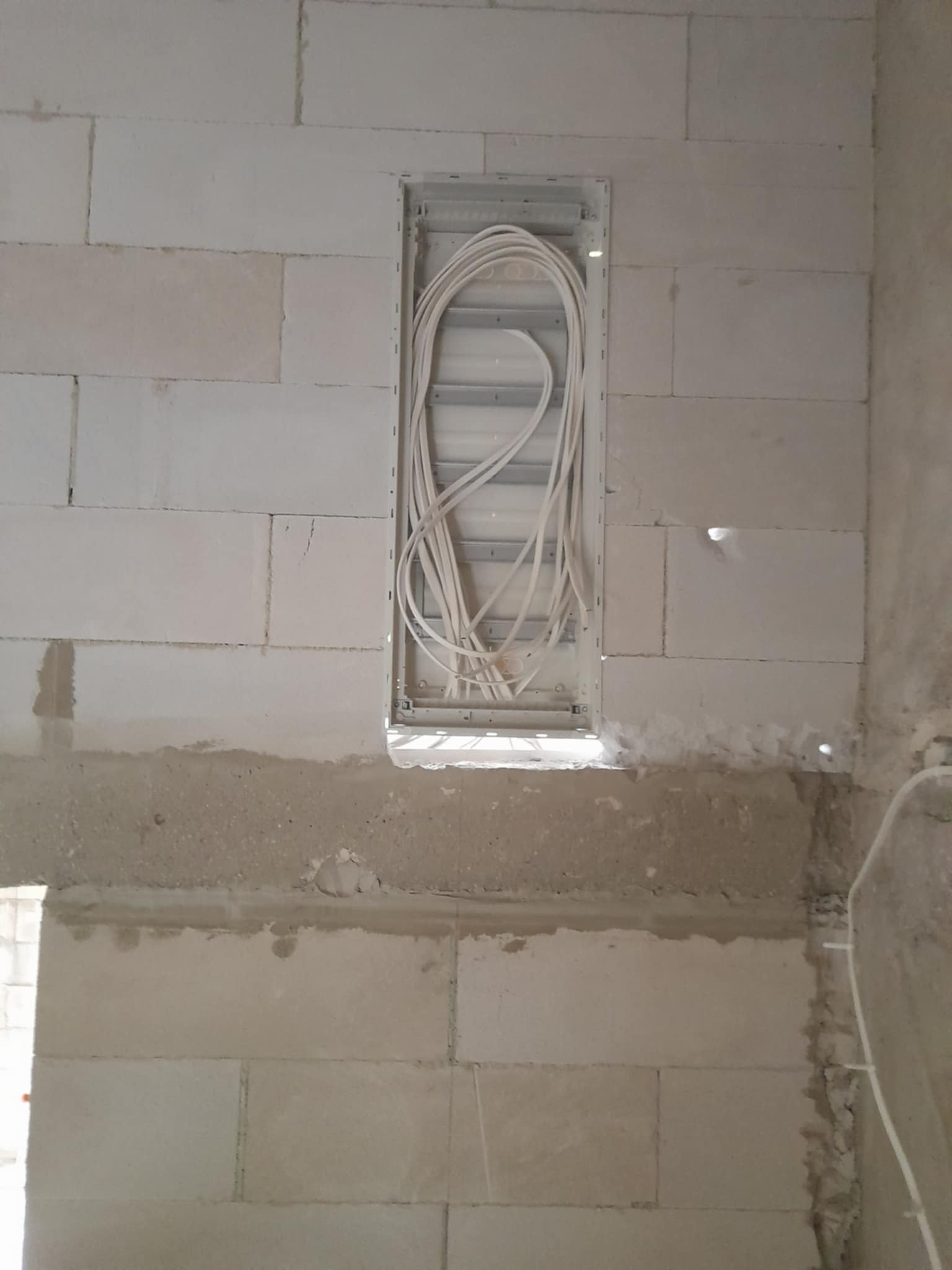 Puszka z przewodami w ścianie z bloczków, instalacja elektryczna w trakcie realizacji w Koło. Widoczne białe kable ułożone w metalowej obudowie.