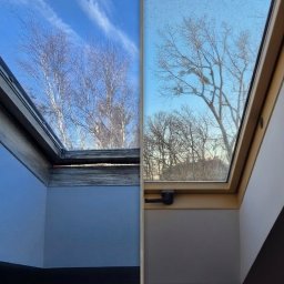 Serwis i naprawa okien Jakub Jewuła - Okno dachowe przed i po czyszczeniu, widok na błękitne niebo z chmurami i drzewa. Po lewej okno czyste, po prawej zabrudzone. Widoczna rama okienna i fragment wnętrza.