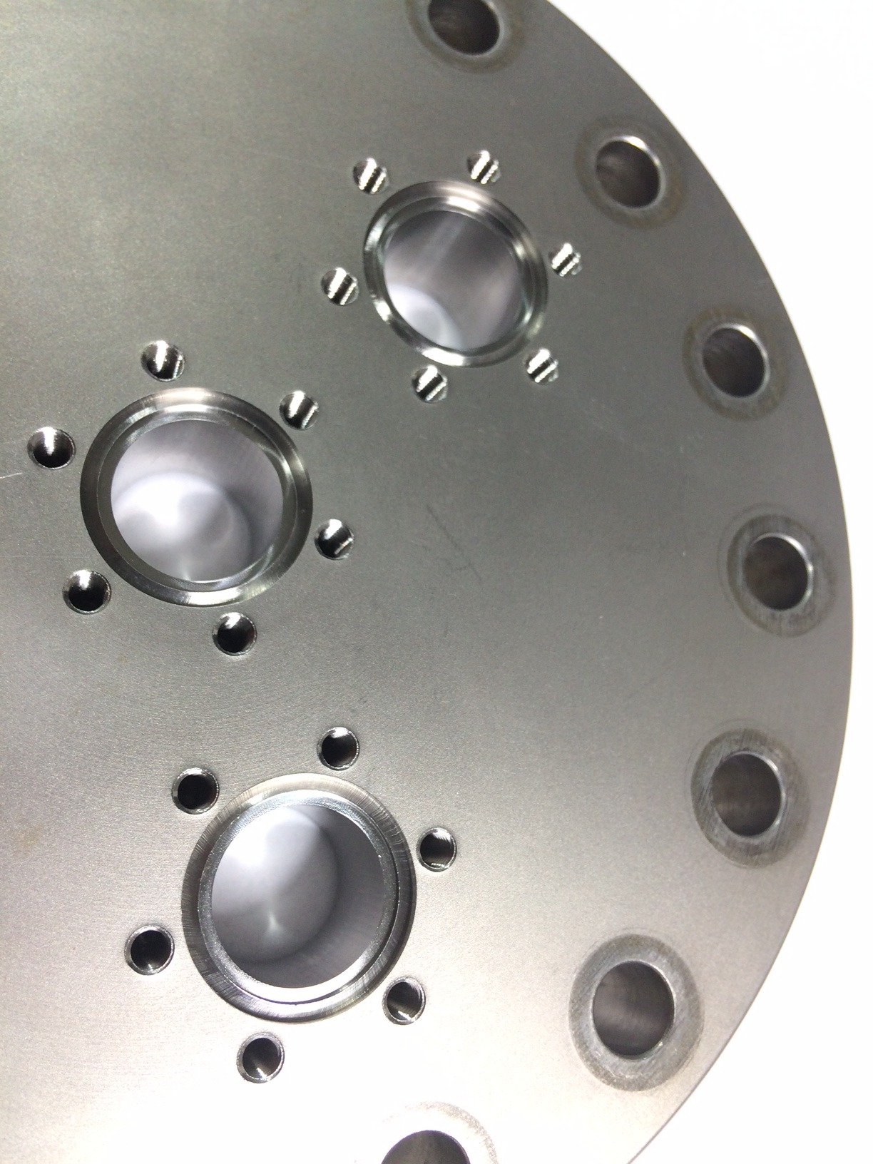 Precyzyjnie obrobiony, metalowy element z otworami o różnych średnicach. Widoczne ślady obróbki skrawaniem. Jasne tło podkreśla detale.