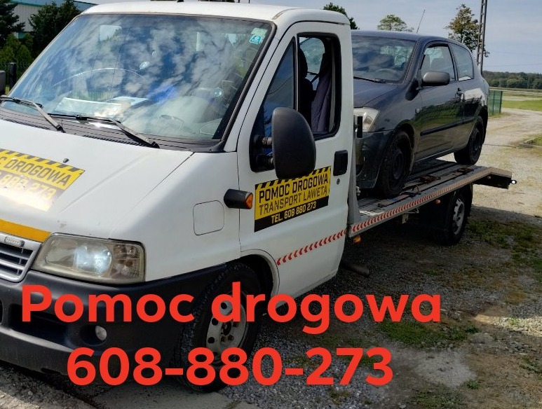 Laweta z czarnym samochodem osobowym na platformie transportowej. Na białej kabinie naklejka z napisem Pomoc Drogowa i numerem telefonu.