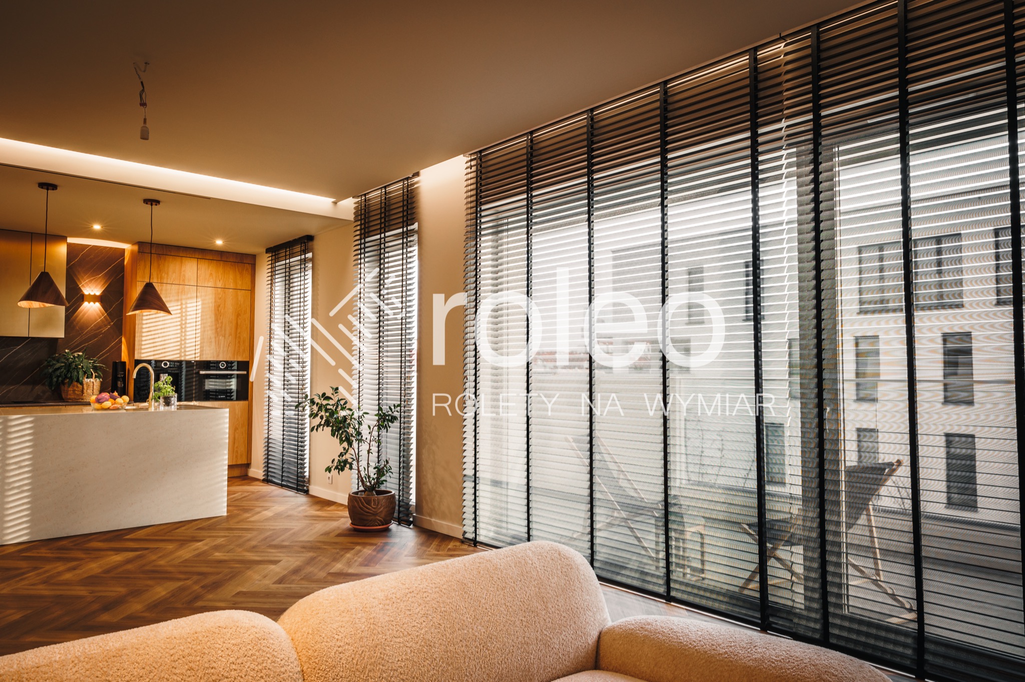 Eleganckie, czarne żaluzje wewnętrzne w luksusowym salonie z parkietem w jodełkę i nowoczesną kuchnią w tle. Widok na zewnątrz przez okno.