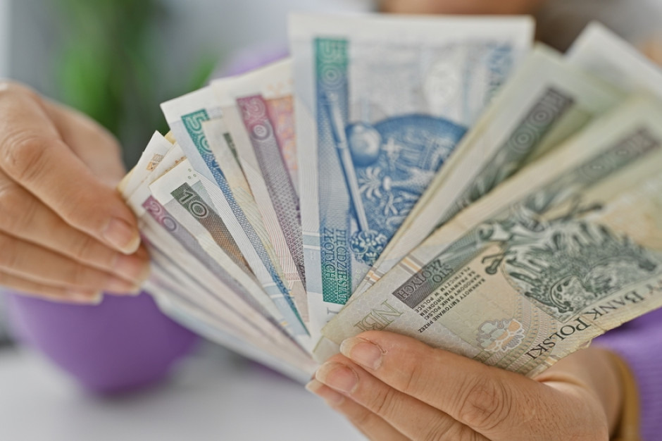 Dłoń trzymająca wachlarz polskich banknotów o różnych nominałach (10, 20, 50, 100 zł) na rozmytym tle. Różnorodność waluty w kontekście finansów.