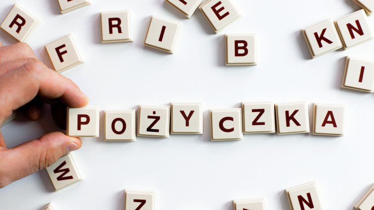 Układanka z liter tworzy słowo 'Pożyczka', dłoń dokłada kolejną literę. Koncepcja finansowa na białym tle.