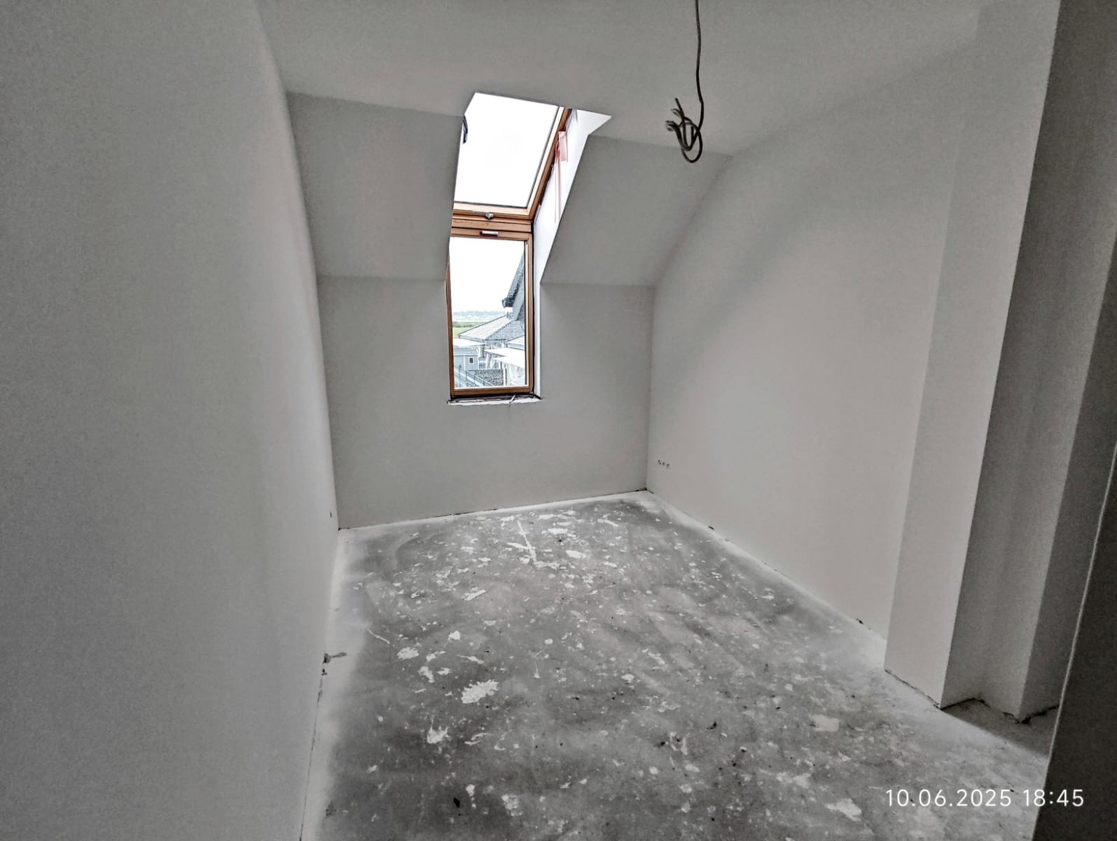 Poddasze po gładziowaniu ścian i wylewce, widoczne okno dachowe i wystające przewody. Ściany pomalowane na biało.