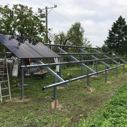 INVICTEL PIKUŁA SPÓŁKA JAWNA - Montaż paneli słonecznych na metalowej konstrukcji w ogrodzie, widoczne narzędzia i drabina. Częściowo zainstalowane panele, w tle drzewa i słupy energetyczne.