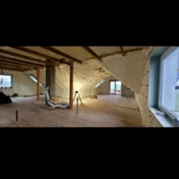 Poddasze z drewnianą podłogą po aplikacji izolacji piankowej na ścianach i suficie, widoczne okno i elementy konstrukcyjne.