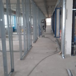 Medbud - Konstrukcja szkieletowa ścian działowych z profili stalowych w surowym wnętrzu, widoczne instalacje i drabina. Etap prac wykończeniowych w obiekcie komercyjnym.