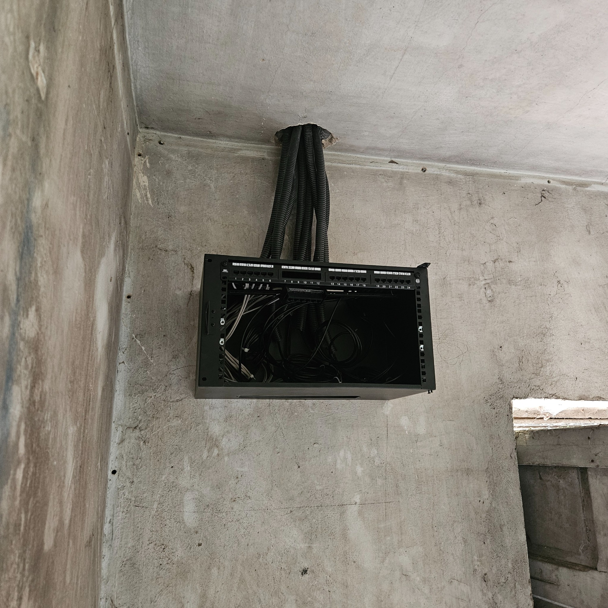 Montaż skrzynki z okablowaniem w surowym wnętrzu. Widoczne kable w peszlach wchodzące do skrzynki. Etap prac instalacyjnych w pomieszczeniu.