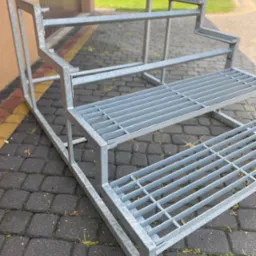 Metalowa konstrukcja schodów z kratownicą, surowy stan, widok z boku na brukowanym podłożu. Schody przygotowane do montażu.