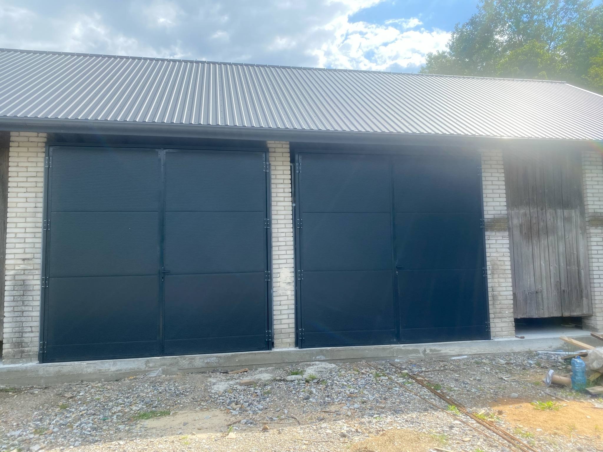 Dwuskrzydłowa, przesuwna brama garażowa z poziomych profili, w kolorze grafitowym, zamontowana w murowanym budynku z blachy trapezowej na dachu.