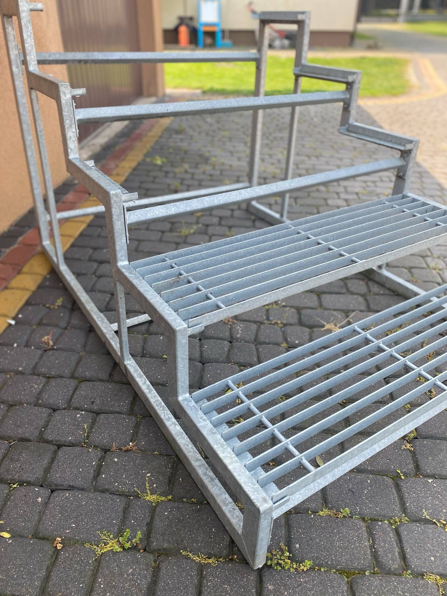 Metalowa konstrukcja schodów z kratownicą, surowy stan, widok z boku na brukowanym podłożu. Schody przygotowane do montażu.