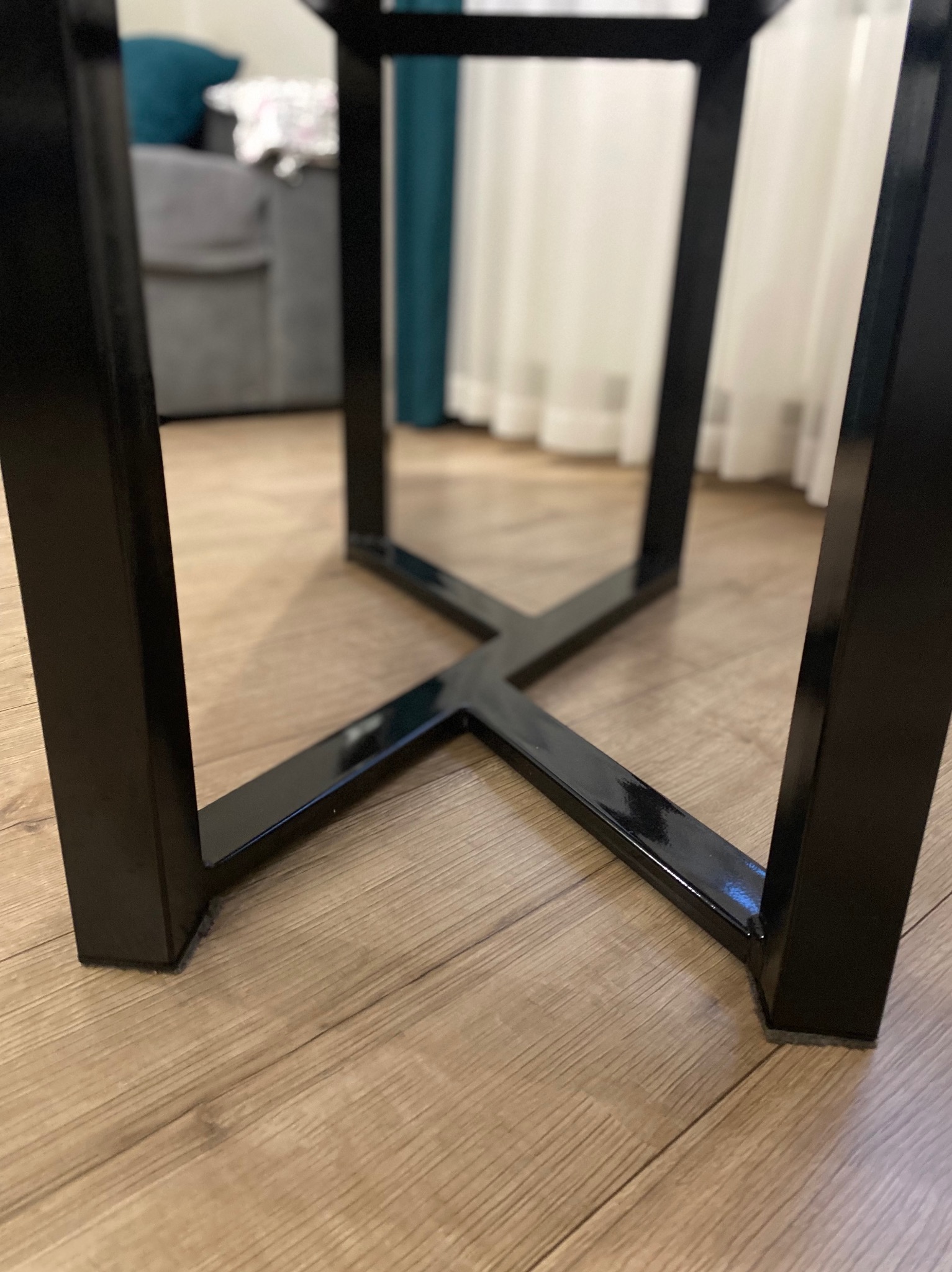Czarna, metalowa podstawa stołu z profili kwadratowych, spawana w kształt litery X, na drewnianej podłodze. Widoczne detale spawów i połyskliwa powierzchnia.