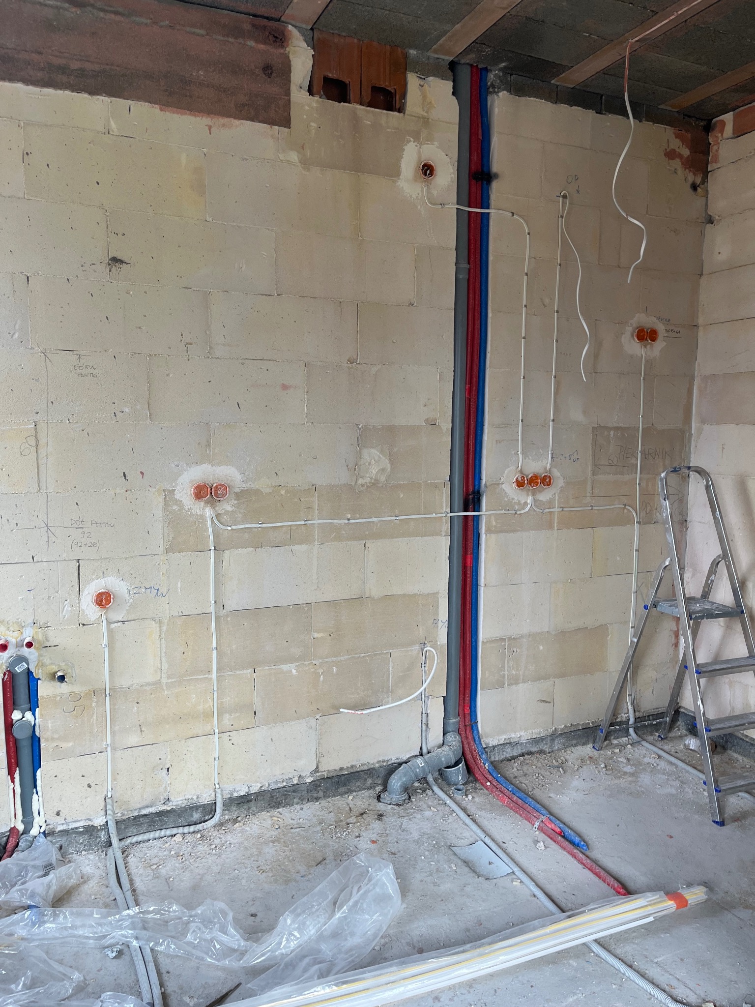 Ściana z instalacją elektryczną i wodno-kanalizacyjną w surowym stanie. Widoczne kable i rury w ścianie z betonu komórkowego, przygotowane do dalszych prac wykończeniowych.
