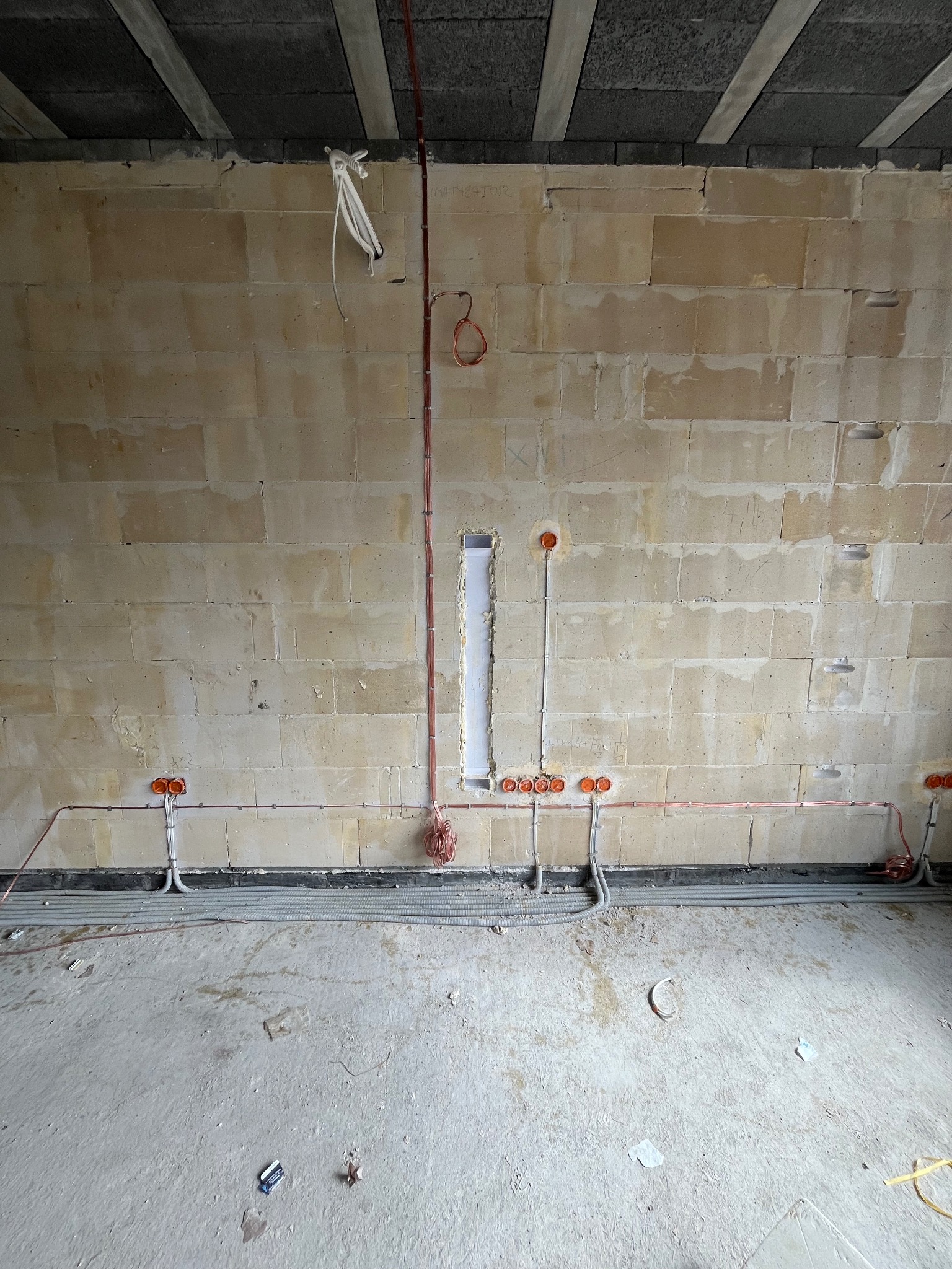 Surowa ściana z instalacją elektryczną w trakcie montażu: kable w peszlach, puszki pod gniazdka i przewody pionowe. Widoczne niedokończone wykończenie wnętrza.