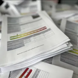 Stos dokumentów świadectw energetycznych ułożonych warstwami, z widocznymi wykresami i tabelami, w neutralnym oświetleniu biurowym.
