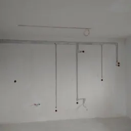 Szare rurki instalacji elektrycznej na ścianie w surowym wnętrzu. Widoczne otwory pod gniazdka i puszki. Instalacja częściowo podtynkowa.