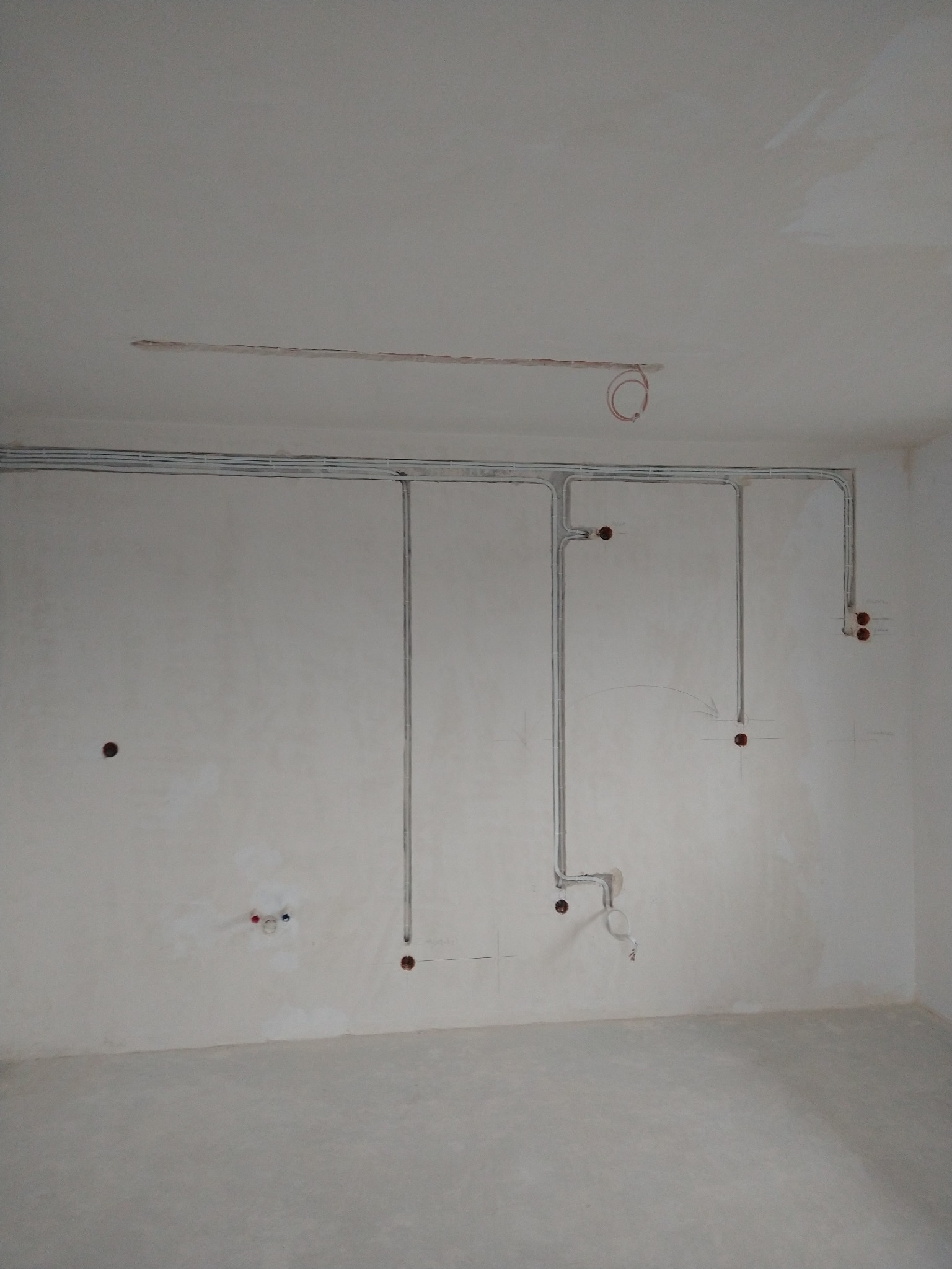Szare rurki instalacji elektrycznej na ścianie w surowym wnętrzu. Widoczne otwory pod gniazdka i puszki. Instalacja częściowo podtynkowa.