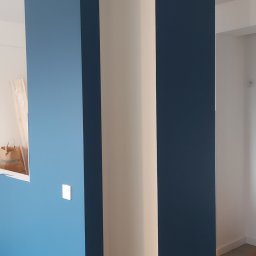 Damian Muchowski - Świeżo pomalowane ściany w odcieniach błękitu i granatu, z białymi elementami wykończeniowymi. Widoczny fragment podłogi z zabezpieczeniem malarskim.