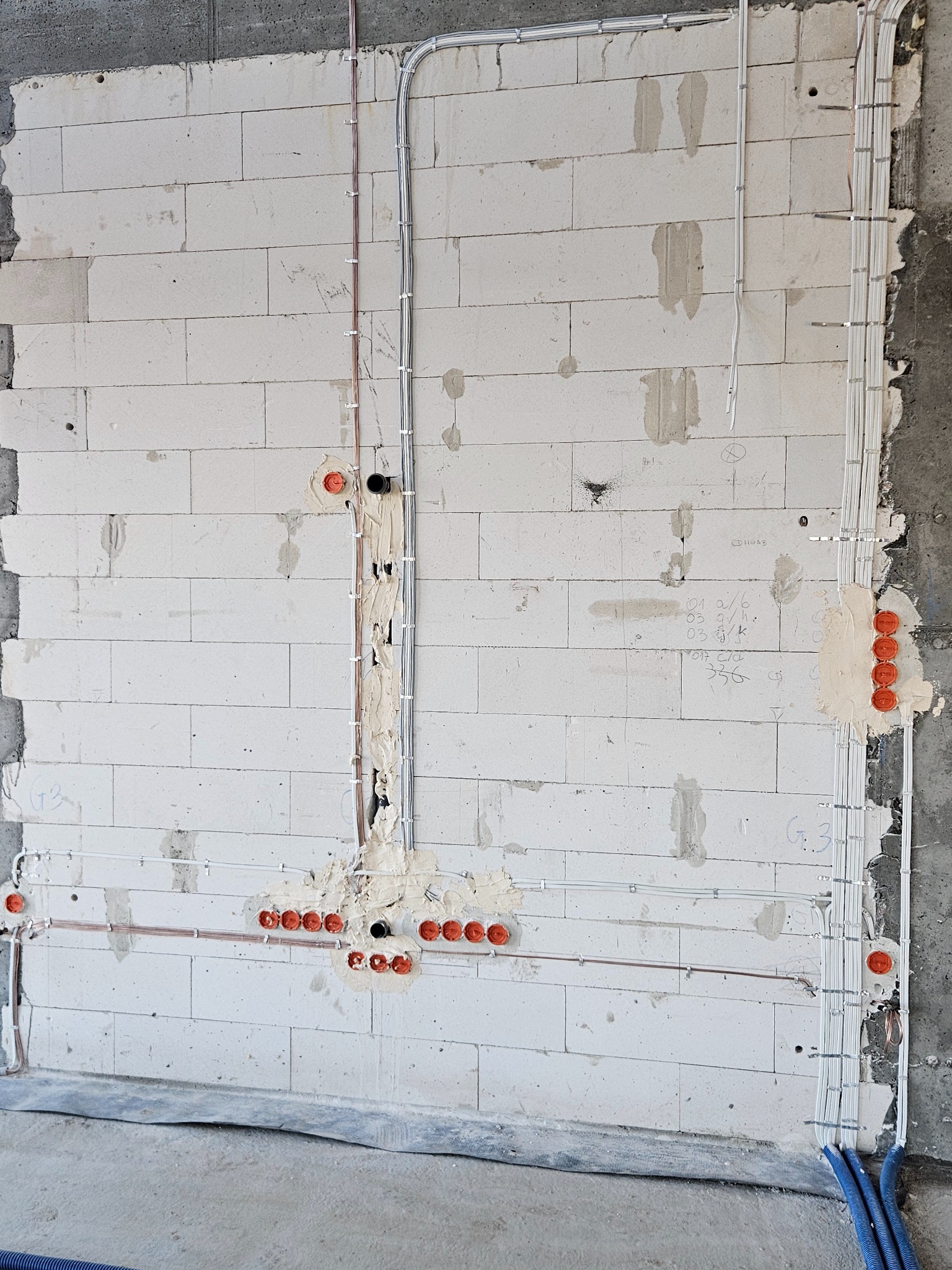 Ściana z betonu komórkowego z zamontowanymi przewodami elektrycznymi w peszlach i puszkami instalacyjnymi, gotowa do dalszych prac wykończeniowych.