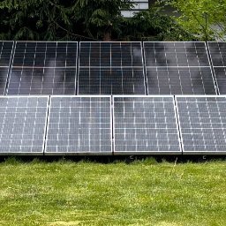 MTech Instalacje S.C. - Dwa rzędy paneli fotowoltaicznych na trawniku, z drzewami w tle. Panele ułożone poziomo, tworząc długą instalację. Widoczne mocowania paneli.