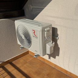 MTech Instalacje S.C. - Zewnętrzna jednostka klimatyzacji Rotenso Versu zamontowana na balkonie z terakotą, widoczna z boku, w słoneczny dzień. Metalowe wsporniki.