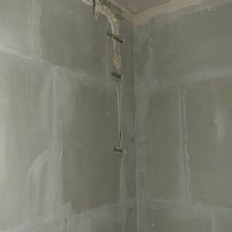 MTech Instalacje S.C. - Montaż instalacji w surowym wnętrzu: rury przymocowane do ściany za pomocą metalowych uchwytów, zabezpieczone pianką montażową przy suficie. Ściany przygotowane do dalszych prac.