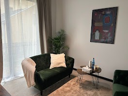 Nowoczesny gabinet z zieloną sofą, stolikiem z chusteczkami i wodą. Na ścianie abstrakcyjny obraz. Stonowana kolorystyka i minimalistyczny wystrój wnętrza.