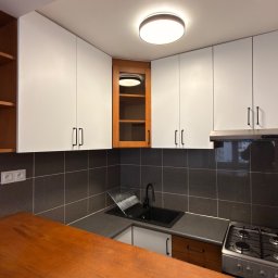 Sanitaro I Firma sprzątająca - Nowoczesna kuchnia po remoncie: białe szafki, ciemne płytki, drewniany blat i czarny zlew. Widok na czystą, uporządkowaną przestrzeń.