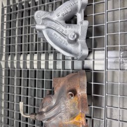 Szymon Koblowski - Dwie metalowe części na kratce: górna po piaskowaniu, srebrna i czysta; dolna zardzewiała, przed czyszczeniem. Widoczne detale i napisy na elementach.