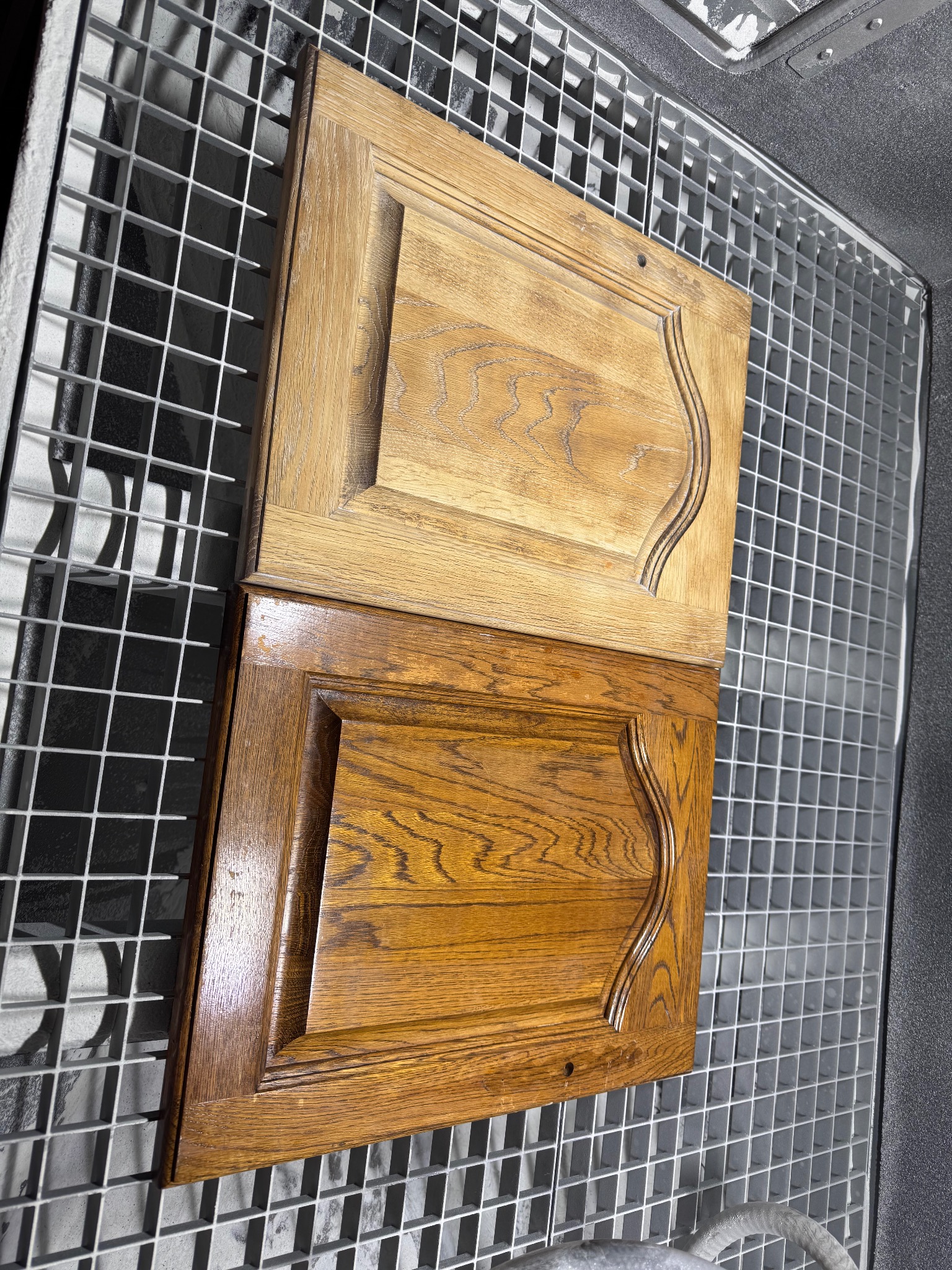 Dwie drewniane fronty meblowe, górna surowa, dolna po bejcowaniu, ułożone na metalowej kratce. Widoczna różnica w odcieniu drewna po zabiegu.