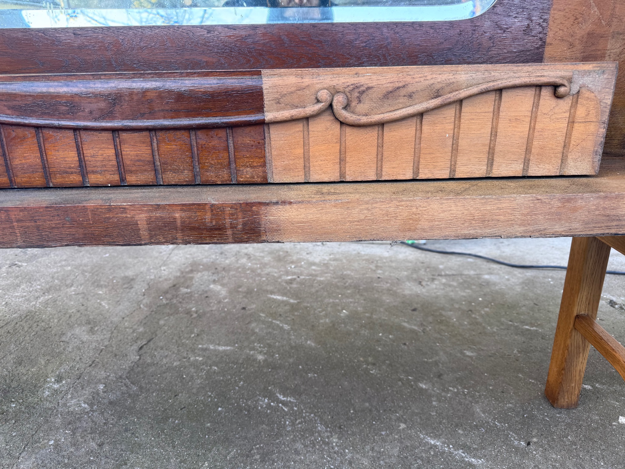 Renowacja drewnianego mebla: fragment z widocznym podziałem na odnowioną, ciemniejszą część i surową, jaśniejszą. Detale zdobień i struktura drewna wyraźnie widoczne.