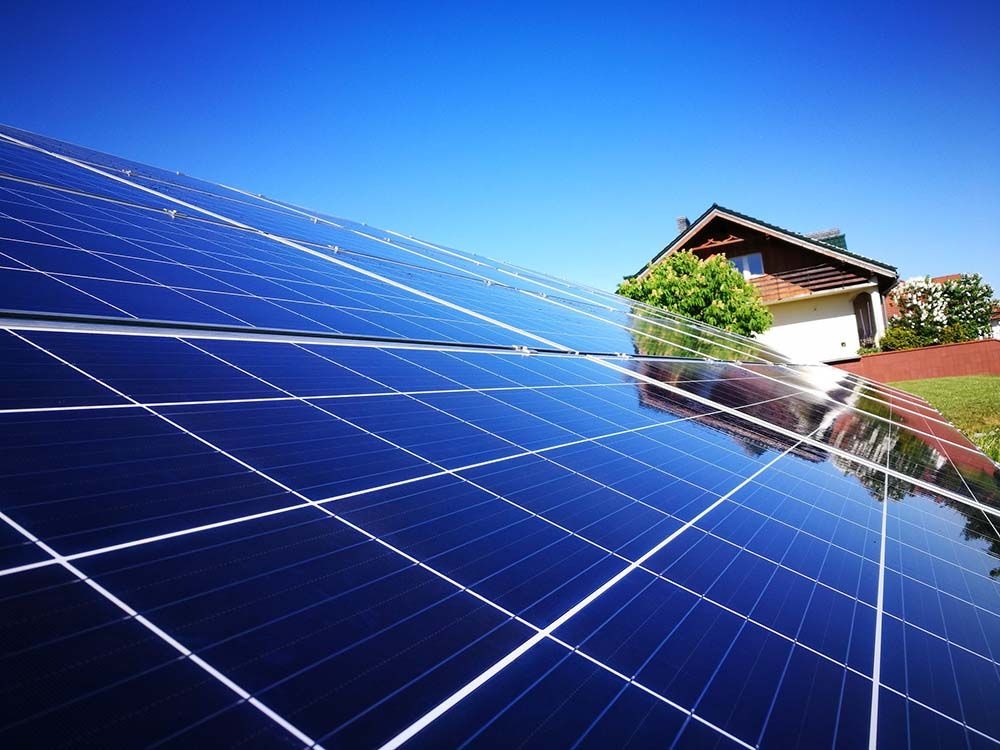 Błękitne panele słoneczne na dachu domu w słoneczny dzień. Widoczne odbicie budynku w panelach. Ekologiczne źródło energii.