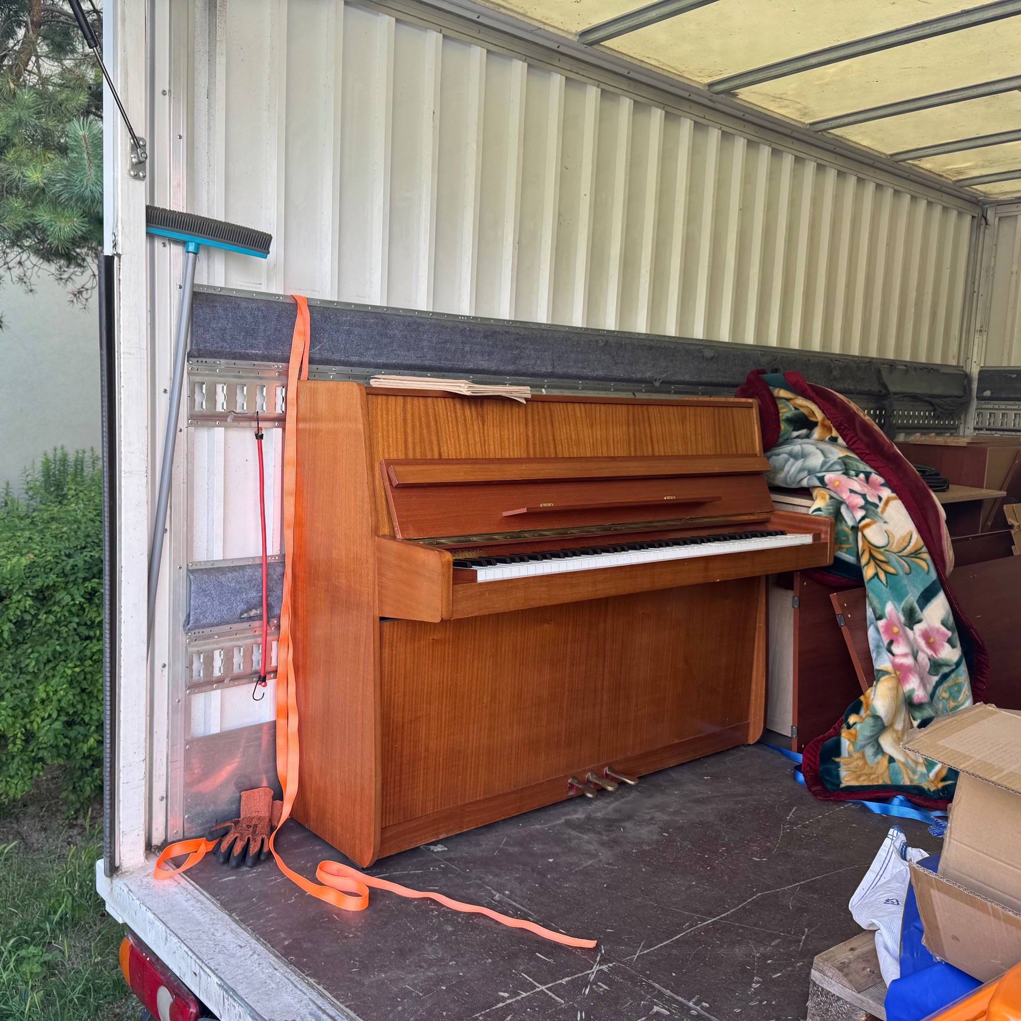 Pianino zabezpieczone pasami wewnątrz pojazdu transportowego w Lublinie, gotowe do przewozu. Widoczna miotła i kartony.