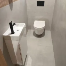 Nowoczesna łazienka z podwieszaną toaletą i umywalką z czarną armaturą na tle szarych płytek i drewnianej boazerii.