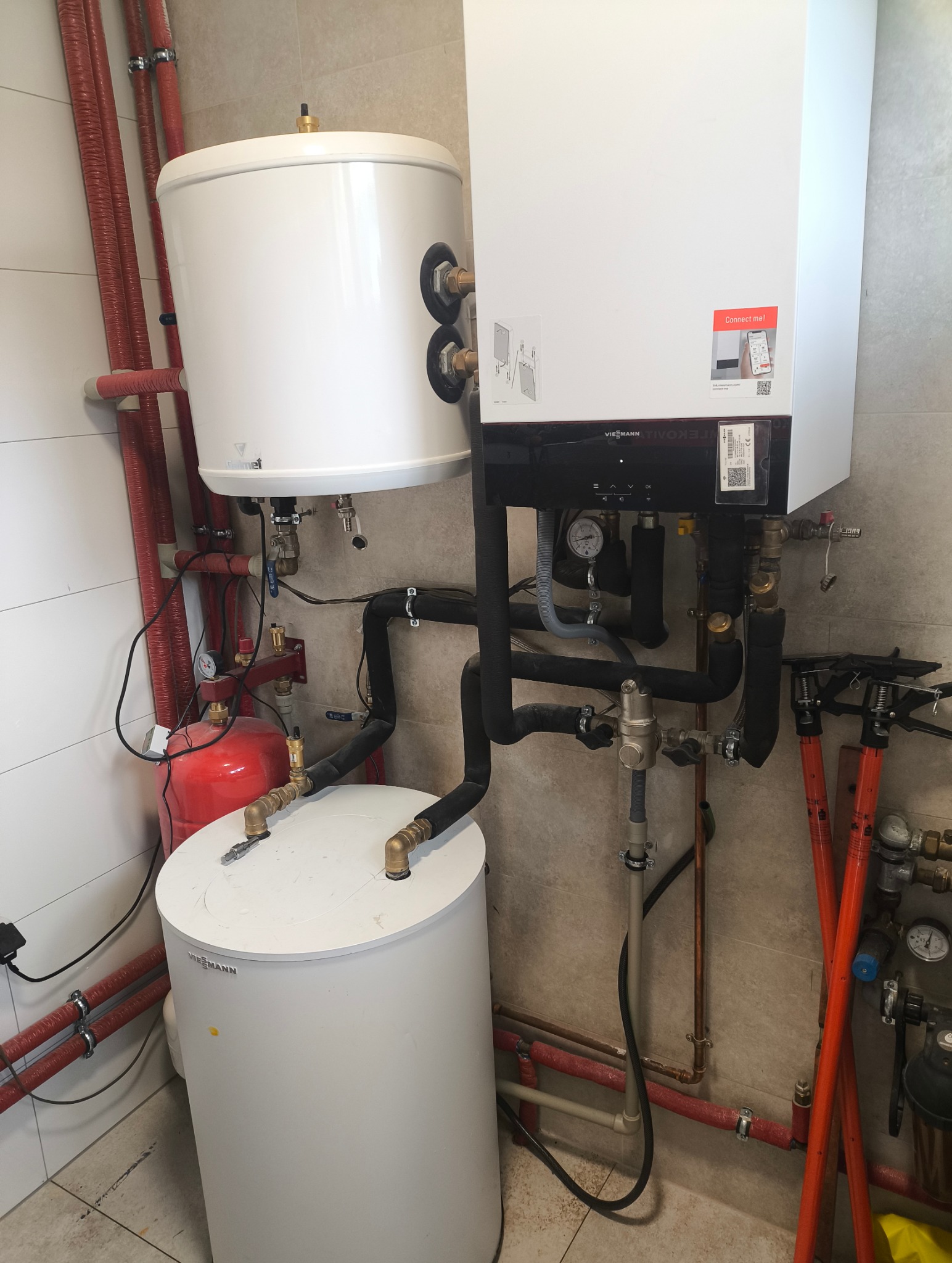 Biały piec gazowy Viessmann z podłączonymi rurami miedzianymi i czarnymi, widoczne także narzędzia monterskie. Instalacja w pomieszczeniu z jasnymi płytkami.